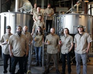 The crew at Barrio Brew Co. standing in front of fermentation tanks